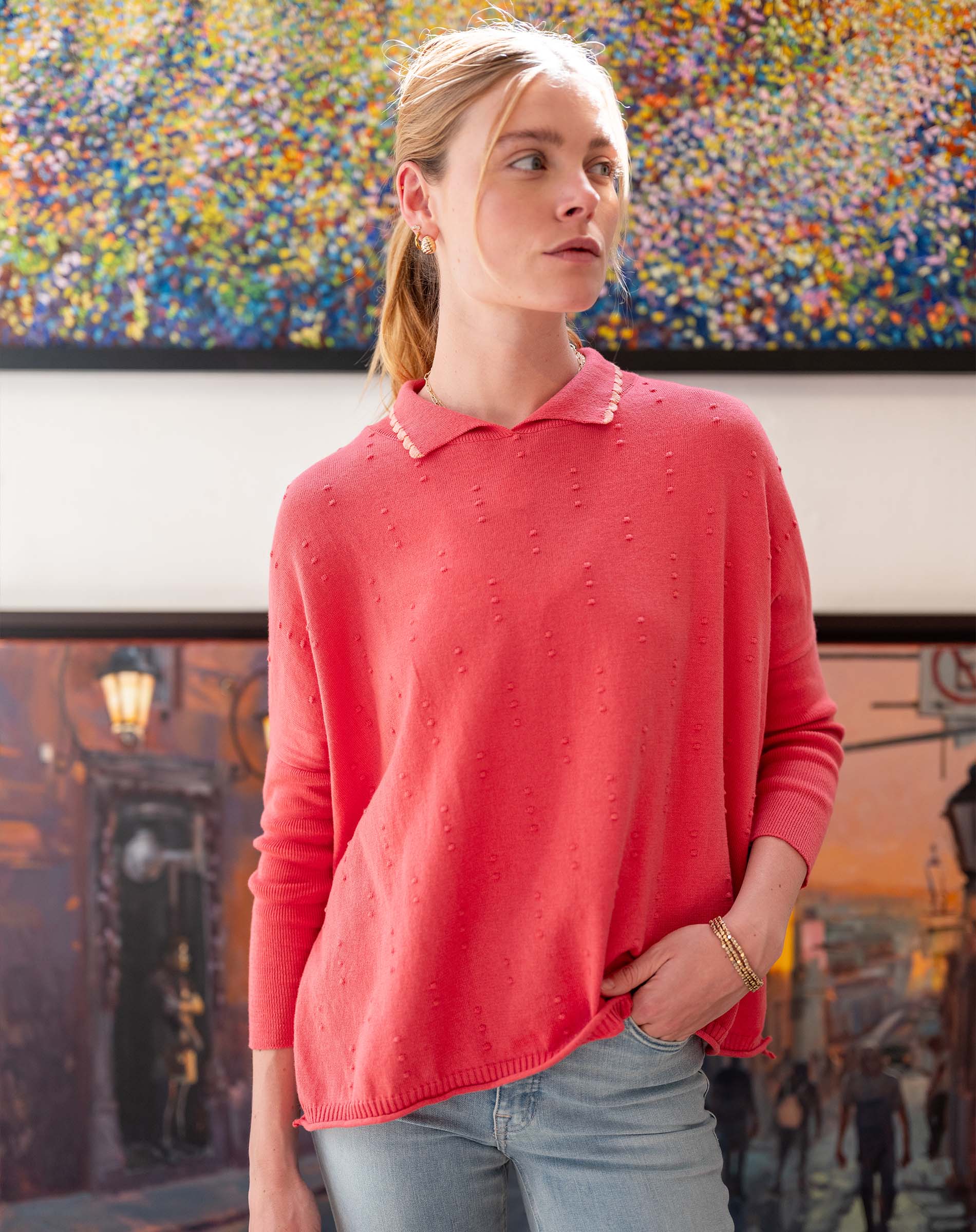 Woman wearing a pink sweater standing in front of a colorful abstract painting