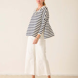 Woman wearing a striped shirt and white pants against a plain background