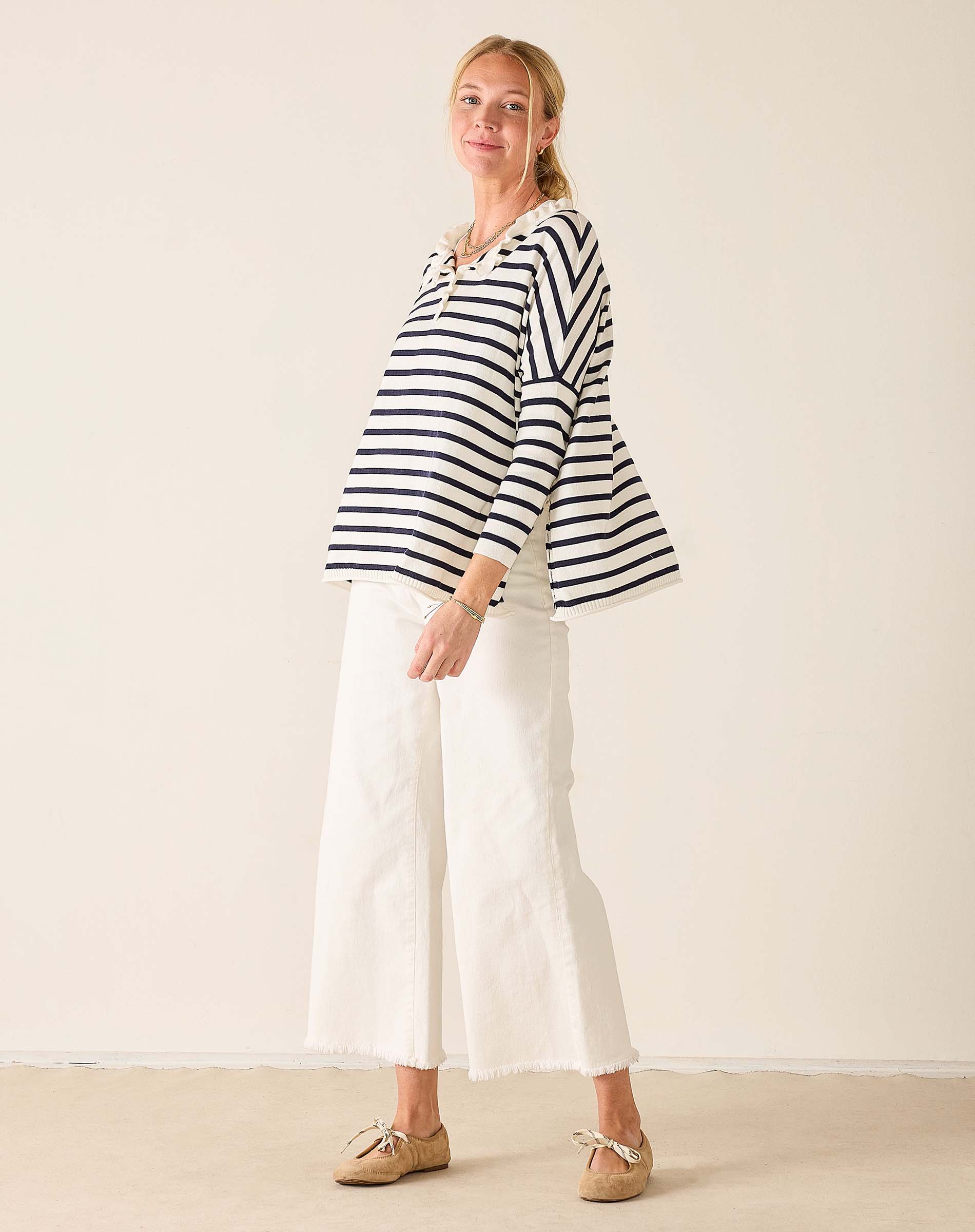 Woman wearing a striped shirt and white pants against a plain background