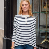 Woman wearing a striped shirt and jeans standing in front of a store entrance.