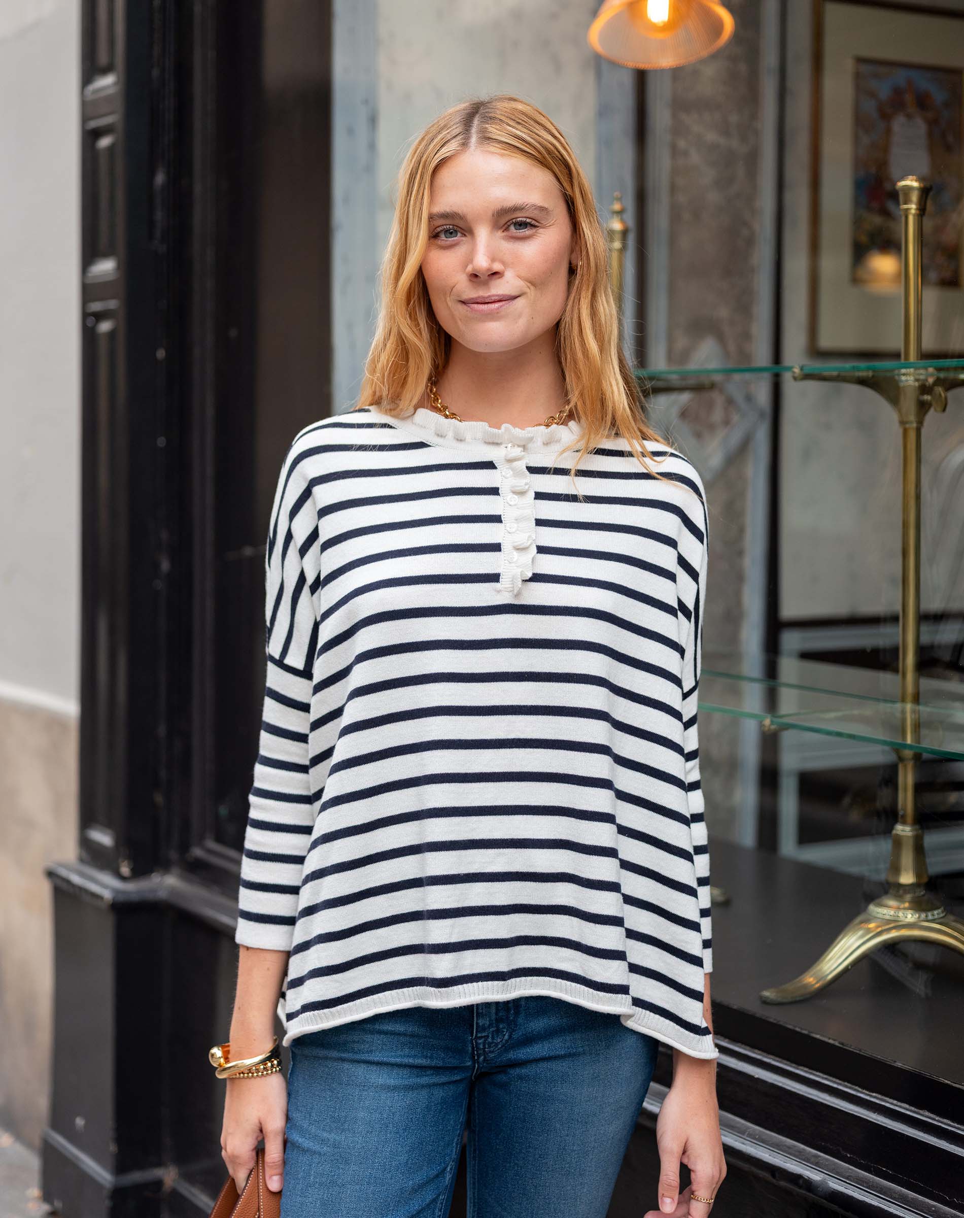 Woman wearing a striped shirt and jeans standing in front of a store entrance.