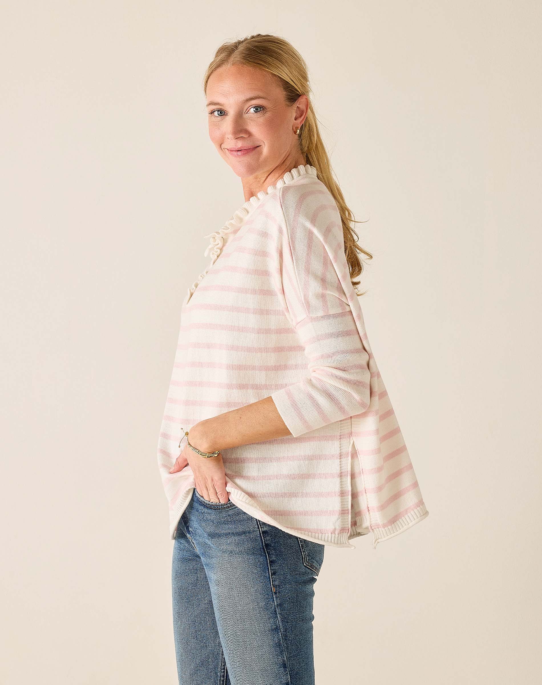 Woman wearing a light pink striped shirt and blue jeans against a plain background