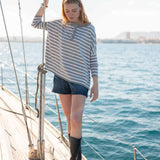 Side view of women's travel-friendly grey striped ruffled henley top worn on a boat in the harbor.