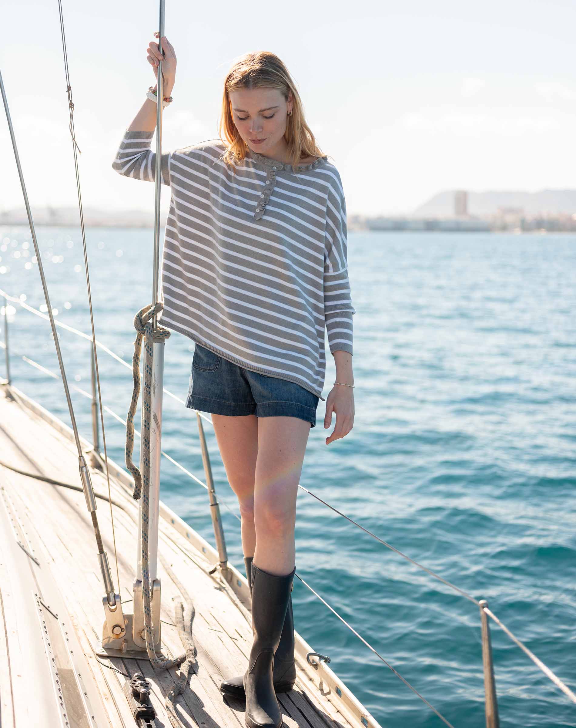 Side view of women's travel-friendly grey striped ruffled henley top worn on a boat in the harbor.