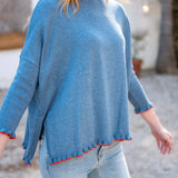 Aegan blue cotton ruffle sweater with vermillion trim and light wash denim jeans.