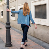 Aegan blue cotton ruffled sweater with a flared hem and dark denim pants.