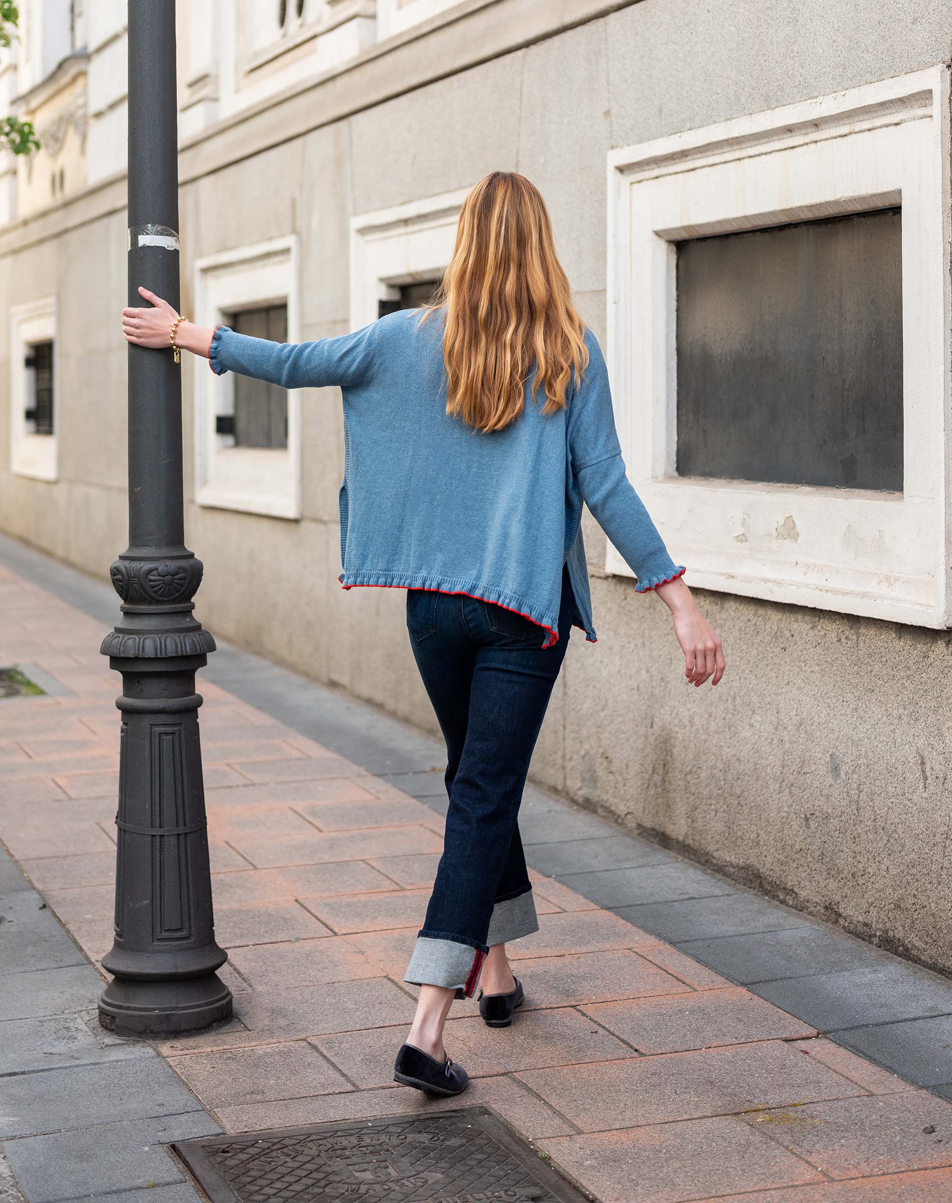 Aegan blue cotton ruffled sweater with a flared hem and dark denim pants.