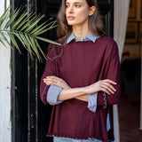 Burgundy cotton ruffle sweater worn over a blue striped button-down shirt and denim jeans.
