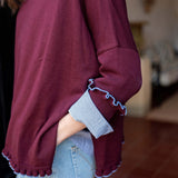 Burgundy knit sweater with a ruffle trim and blue-and-white striped cuffs.