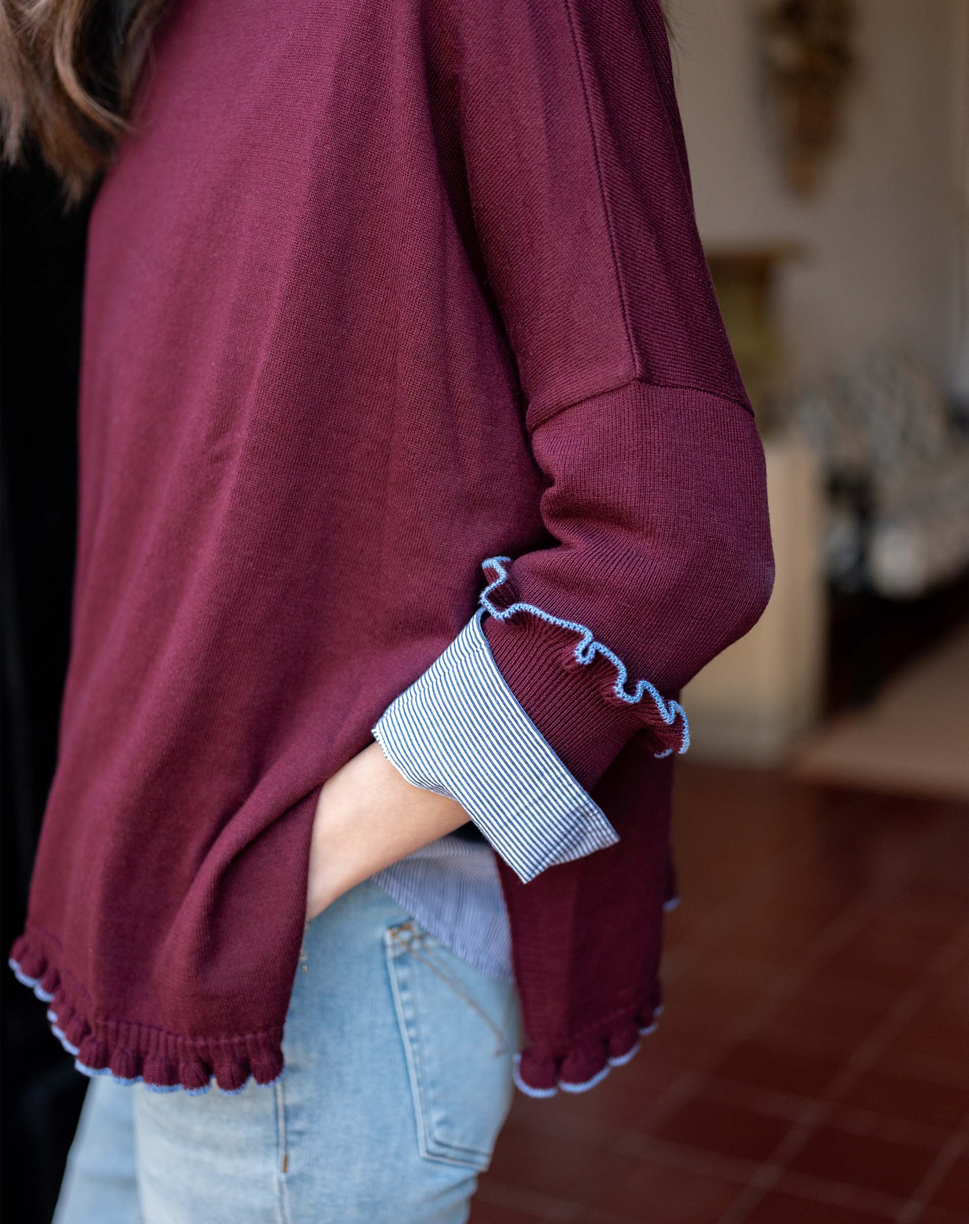 Burgundy knit sweater with a ruffle trim and blue-and-white striped cuffs.