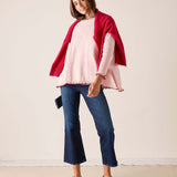 Woman in light orchid ruffled knit sweater and a bordeaux wrap over wide-leg jeans.