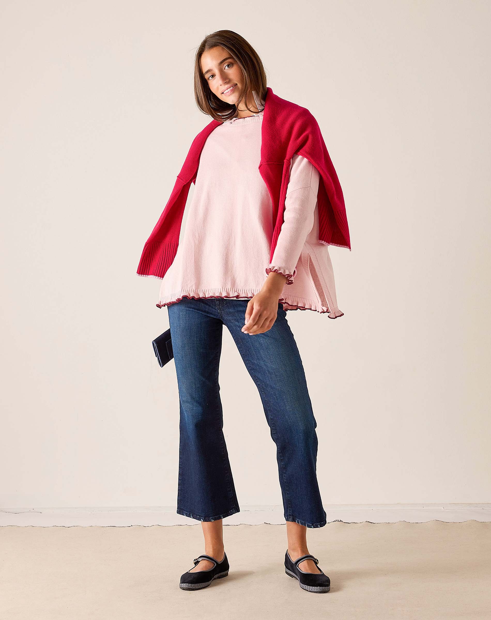 Woman in light orchid ruffled knit sweater and a bordeaux wrap over wide-leg jeans.