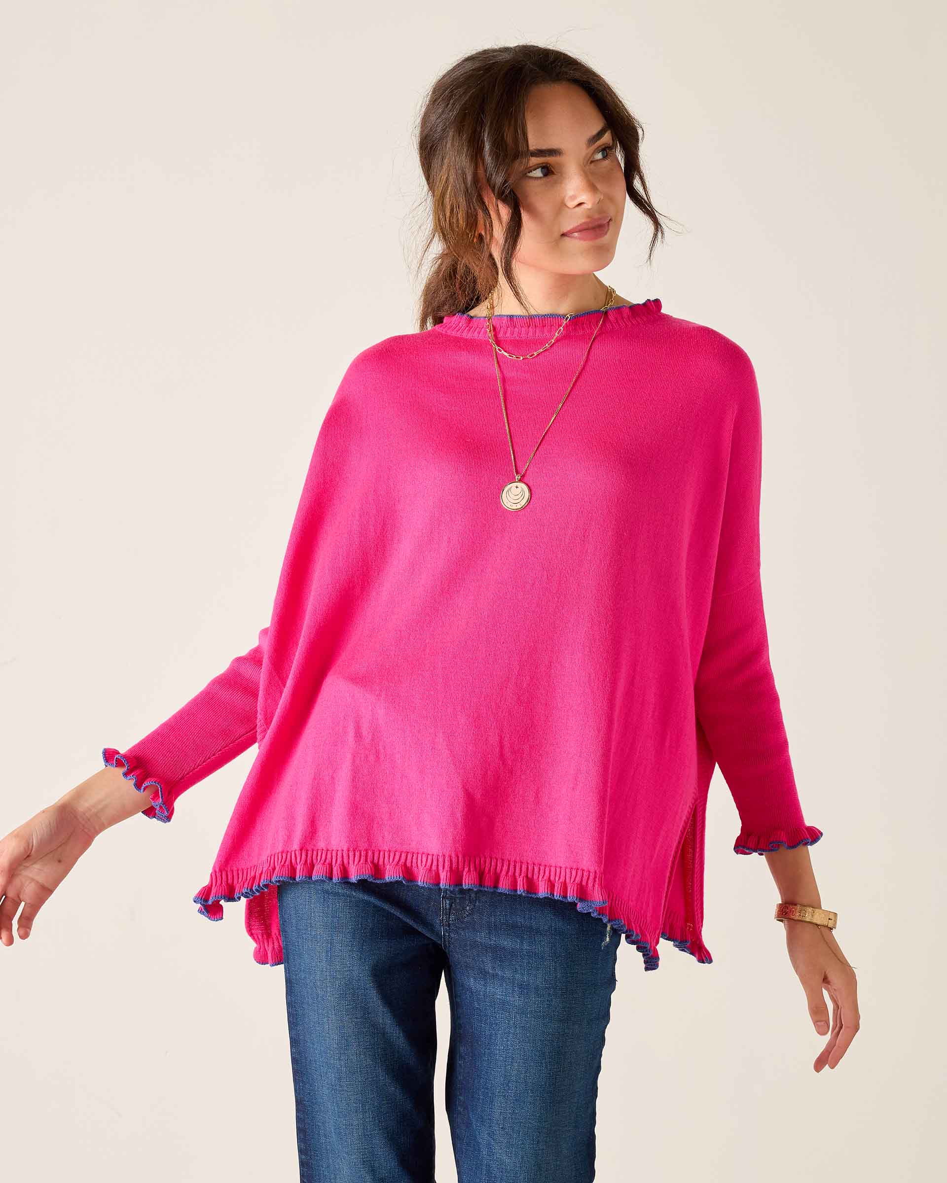 Woman wearing a bright pink sweater with ruffled cuffs and hem on a plain background