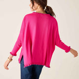 Woman wearing a bright pink sweater and blue jeans on a plain background