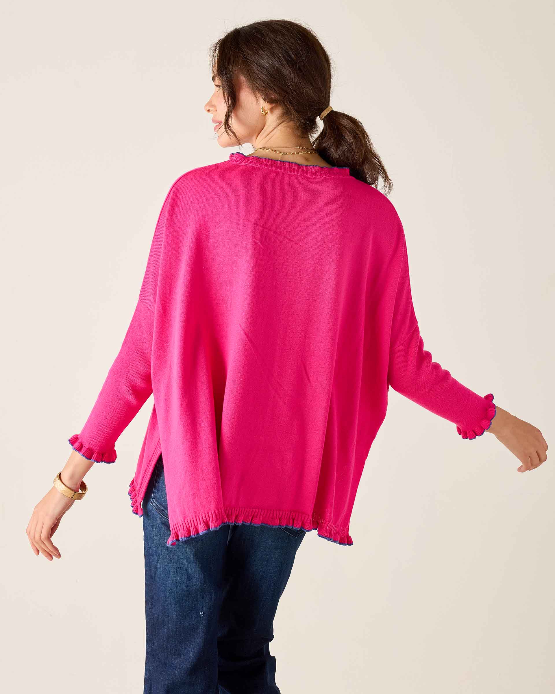Woman wearing a bright pink sweater and blue jeans on a plain background