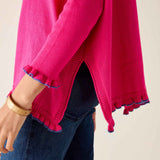 Close-up of a bright pink sweater with ruffled cuffs and hem, worn over dark jeans.