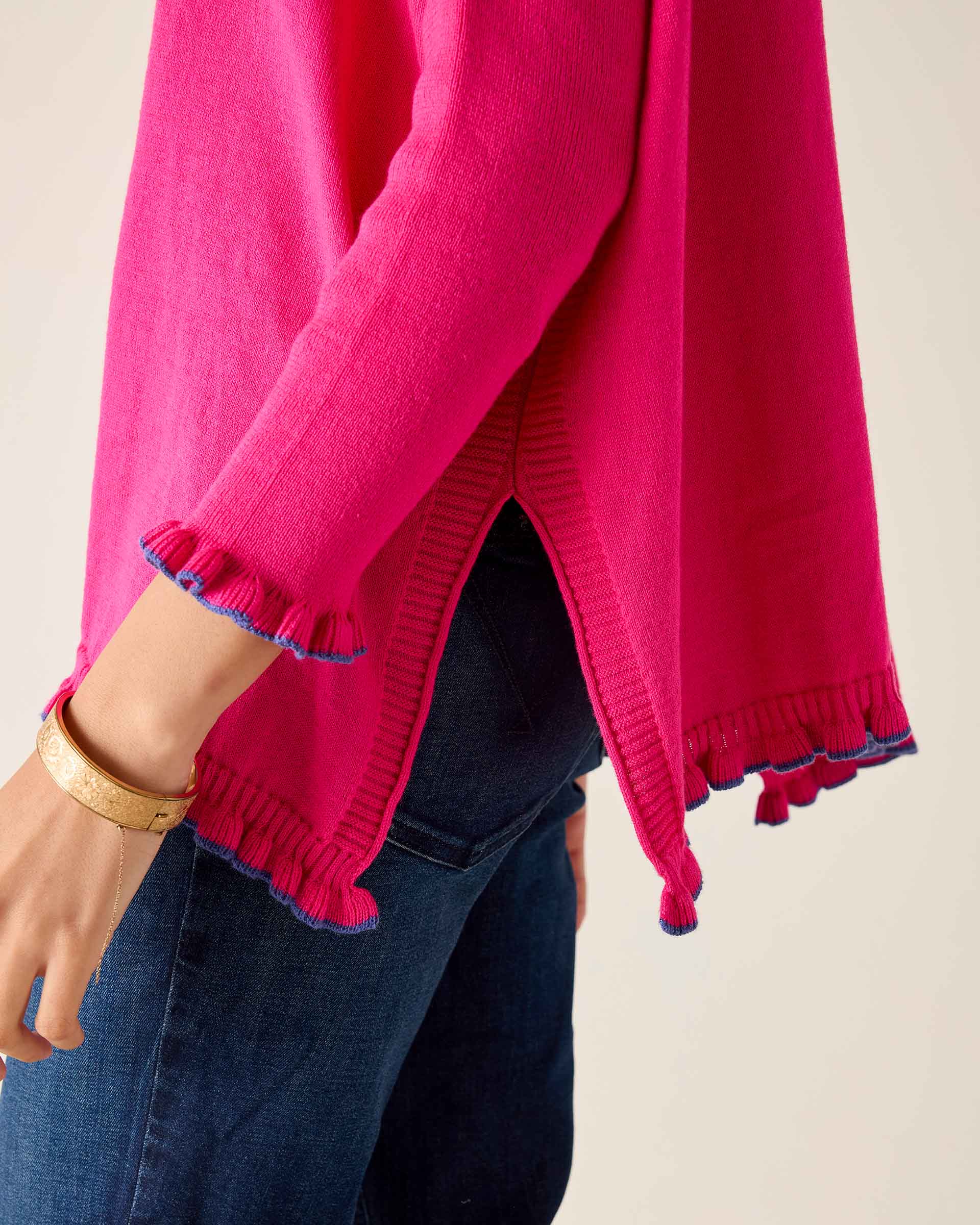 Close-up of a bright pink sweater with ruffled cuffs and hem, worn over dark jeans.