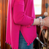 Person wearing a bright pink sweater with blue cuffs and hem, standing indoors.