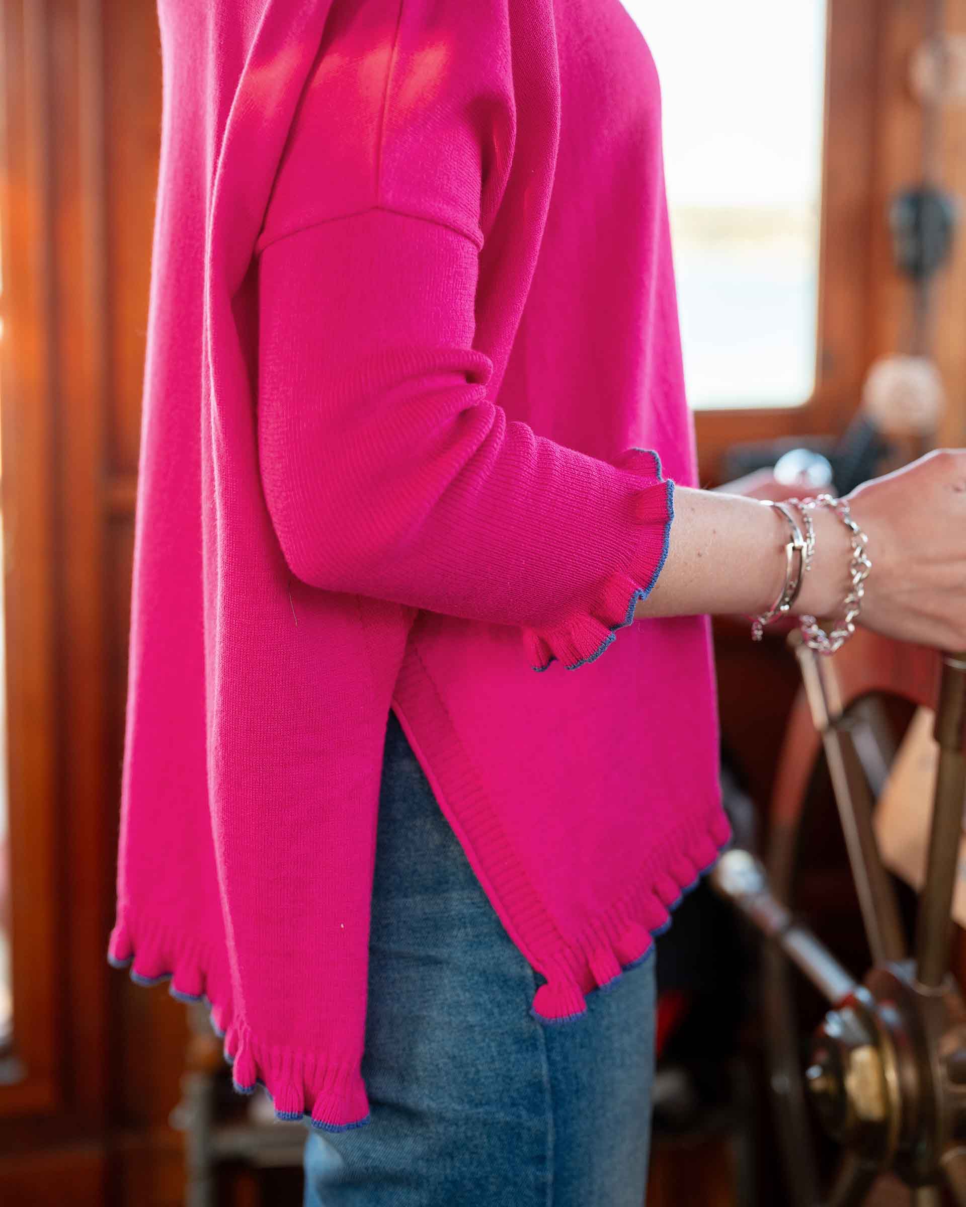Person wearing a bright pink sweater with blue cuffs and hem, standing indoors.