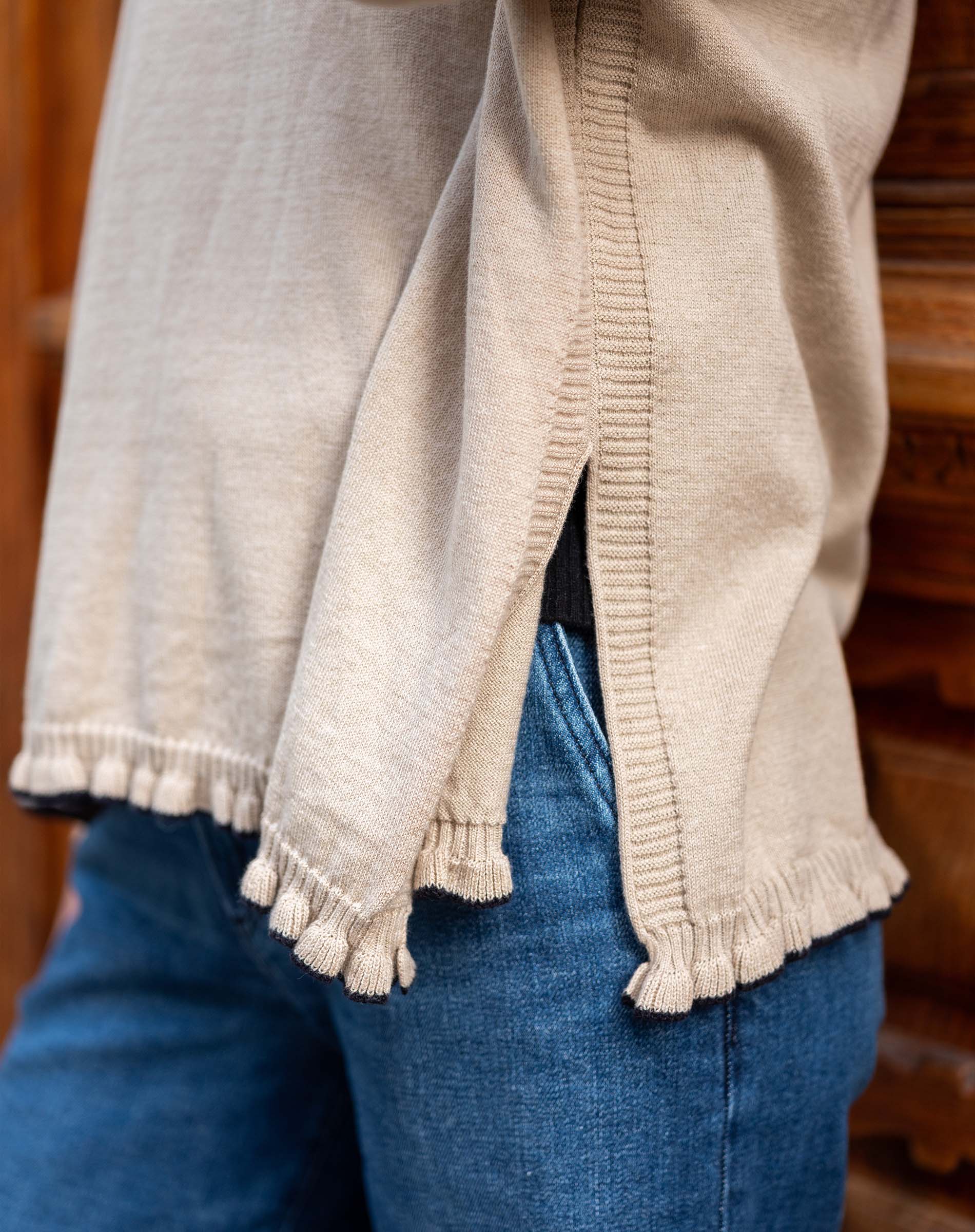 Natural cotton ruffled sweater with a side slit and fringed hem, worn over blue denim jeans.