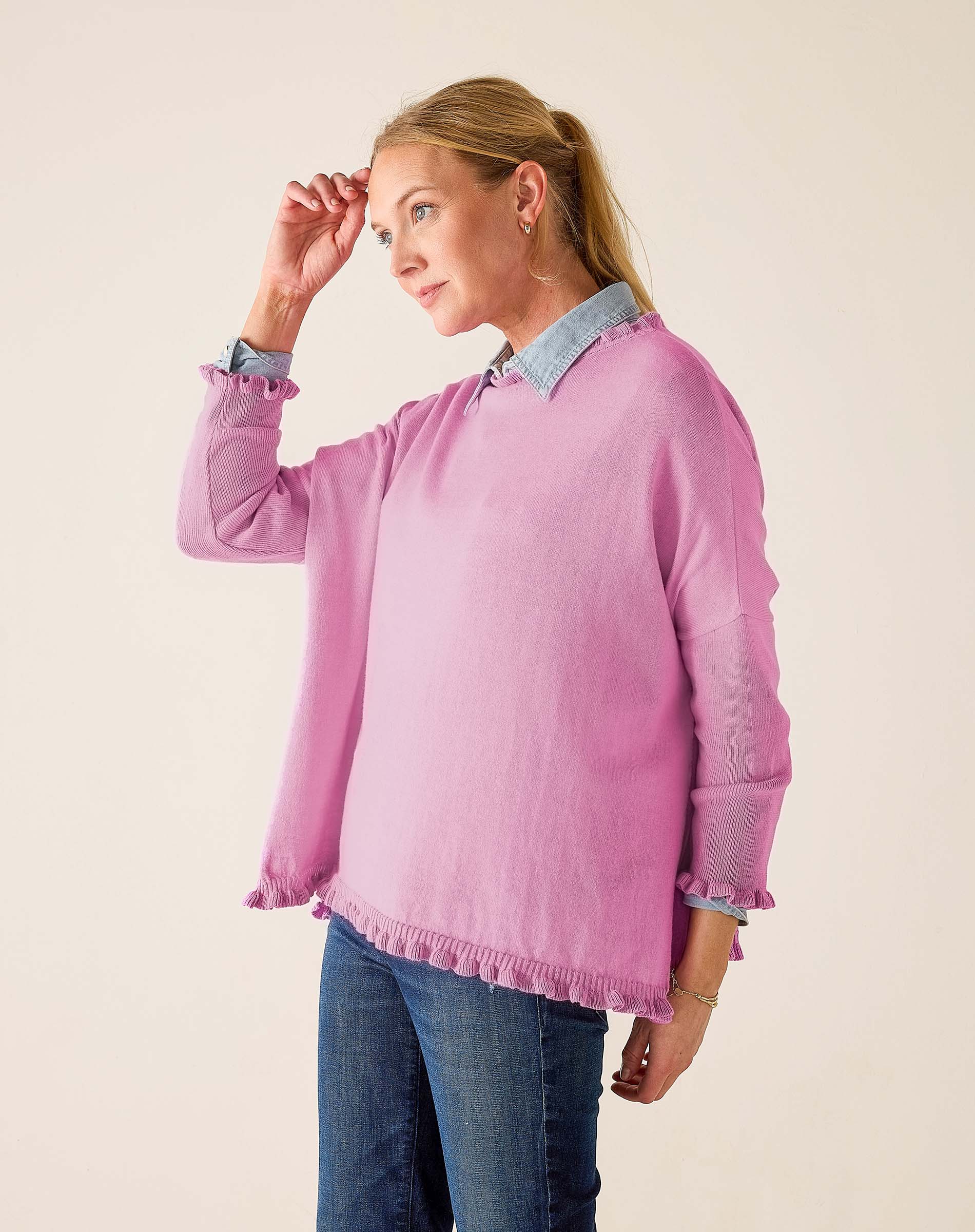 Woman wearing a pink blouse with rolled-up sleeves and blue jeans on a beige background
