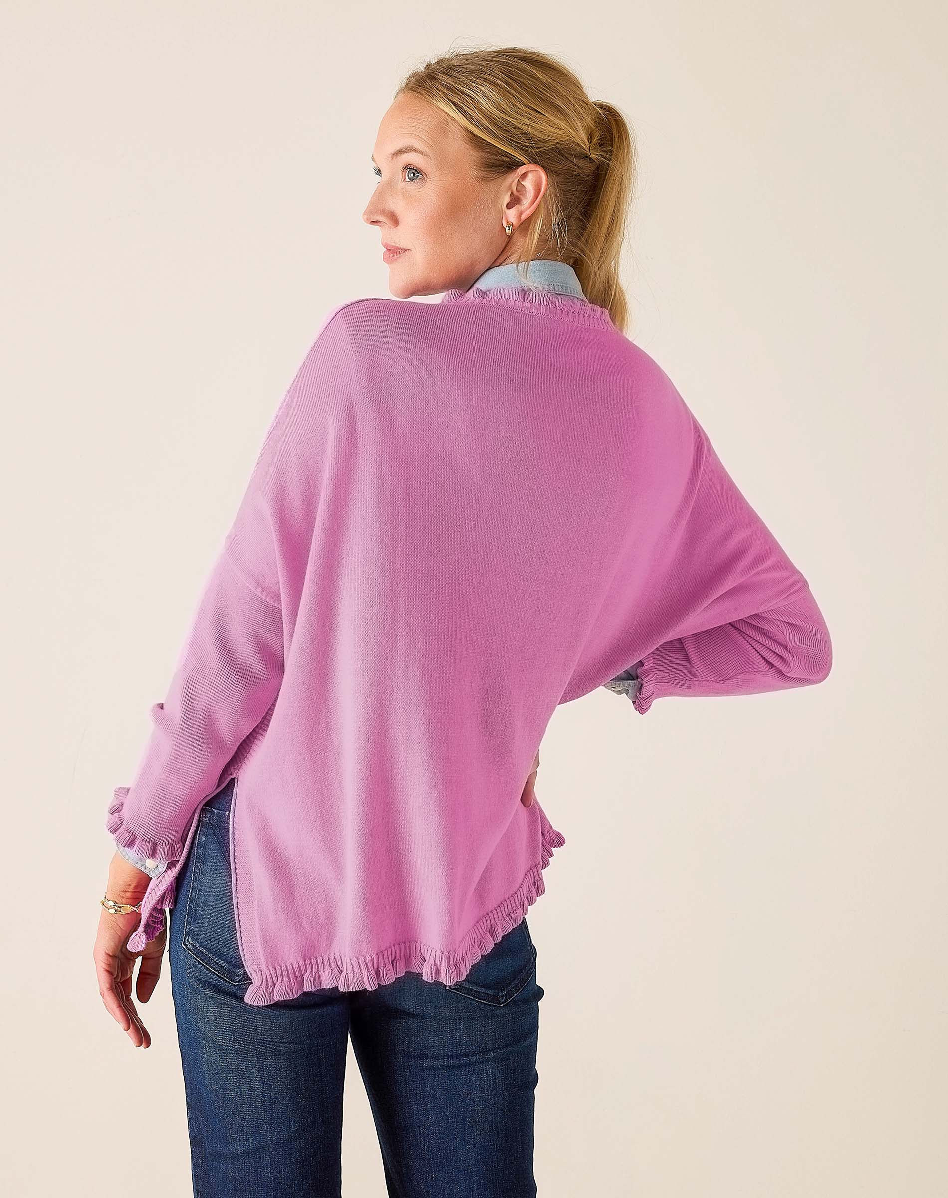 Woman wearing a pink sweater and blue jeans against a plain background