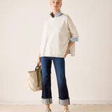 Ladies' travel-ready warm white cotton ruffle sweater over a blue collared shirt with dark wash denim jeans.