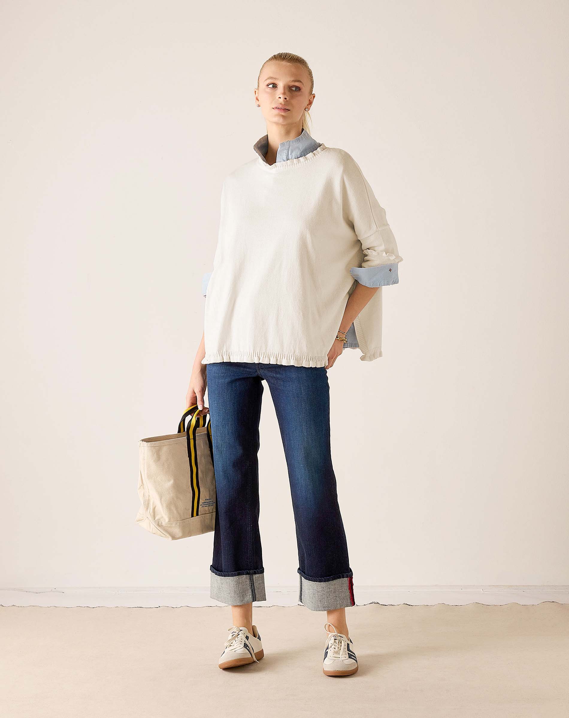 Ladies' travel-ready warm white cotton ruffle sweater over a blue collared shirt with dark wash denim jeans.