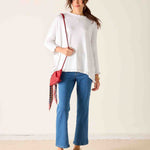 Woman wearing a white top, blue jeans, and brown shoes with a red bag against a beige background