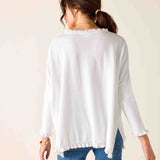 Woman wearing a white long-sleeve top with a subtle pattern on a beige background