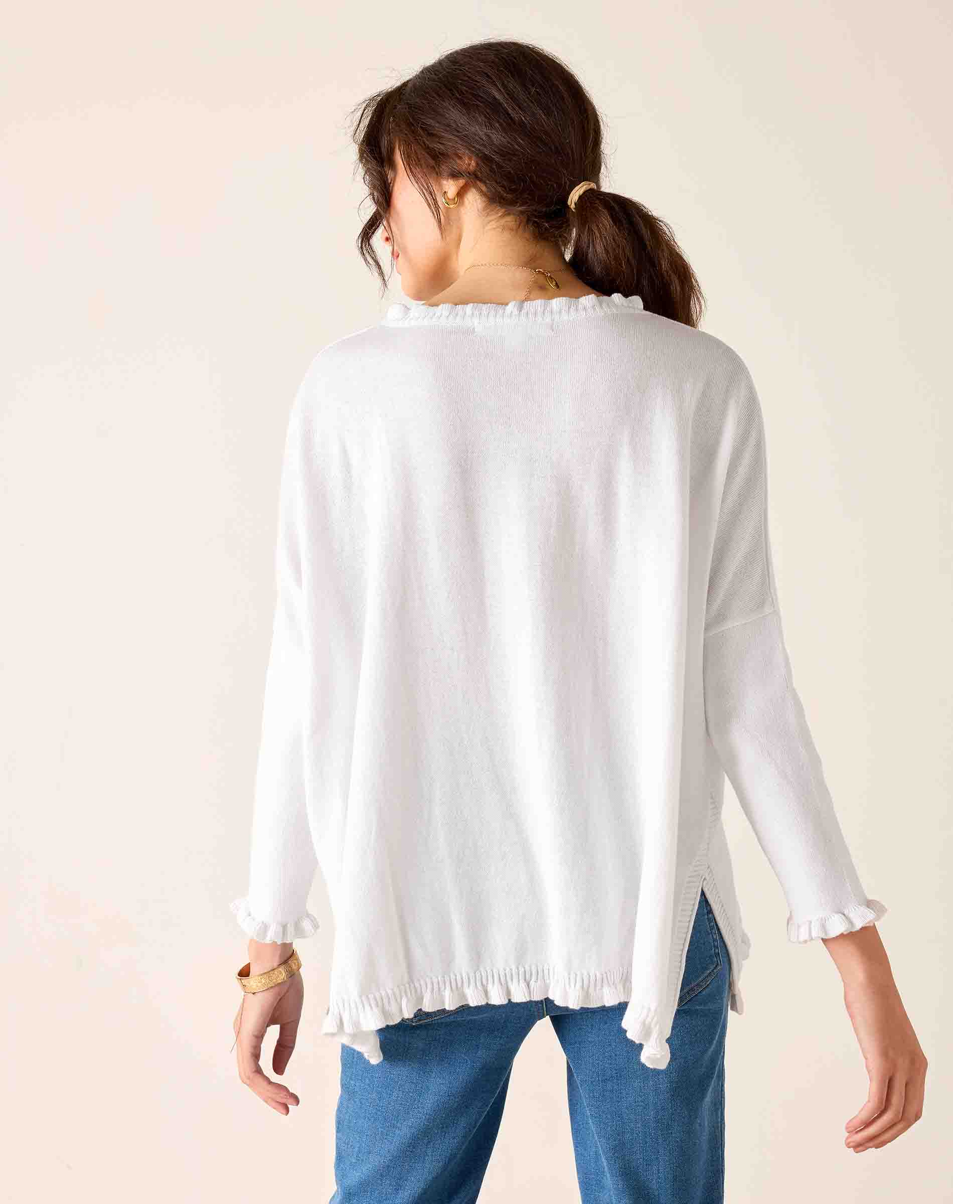 Woman wearing a white long-sleeve top with a subtle pattern on a beige background