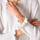 Person wearing a white long-sleeve top with ruffled cuffs and gold jewelry.