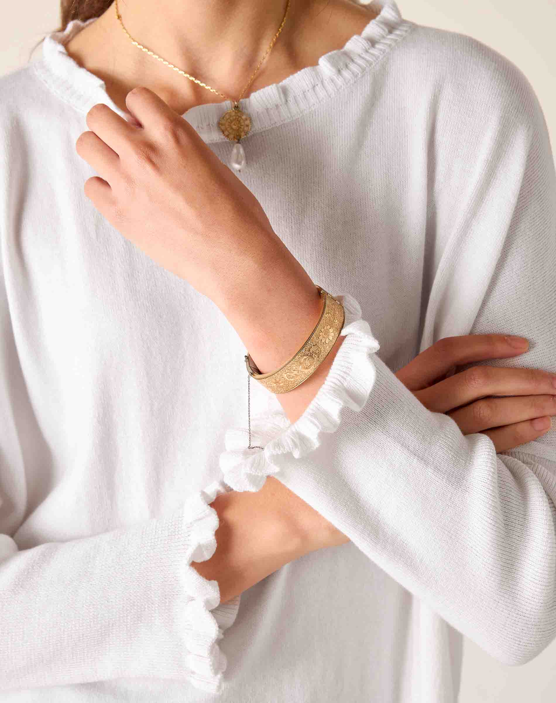 Person wearing a white long-sleeve top with ruffled cuffs and gold jewelry.