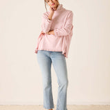 Woman wearing a pink sweater and light blue jeans against a white background