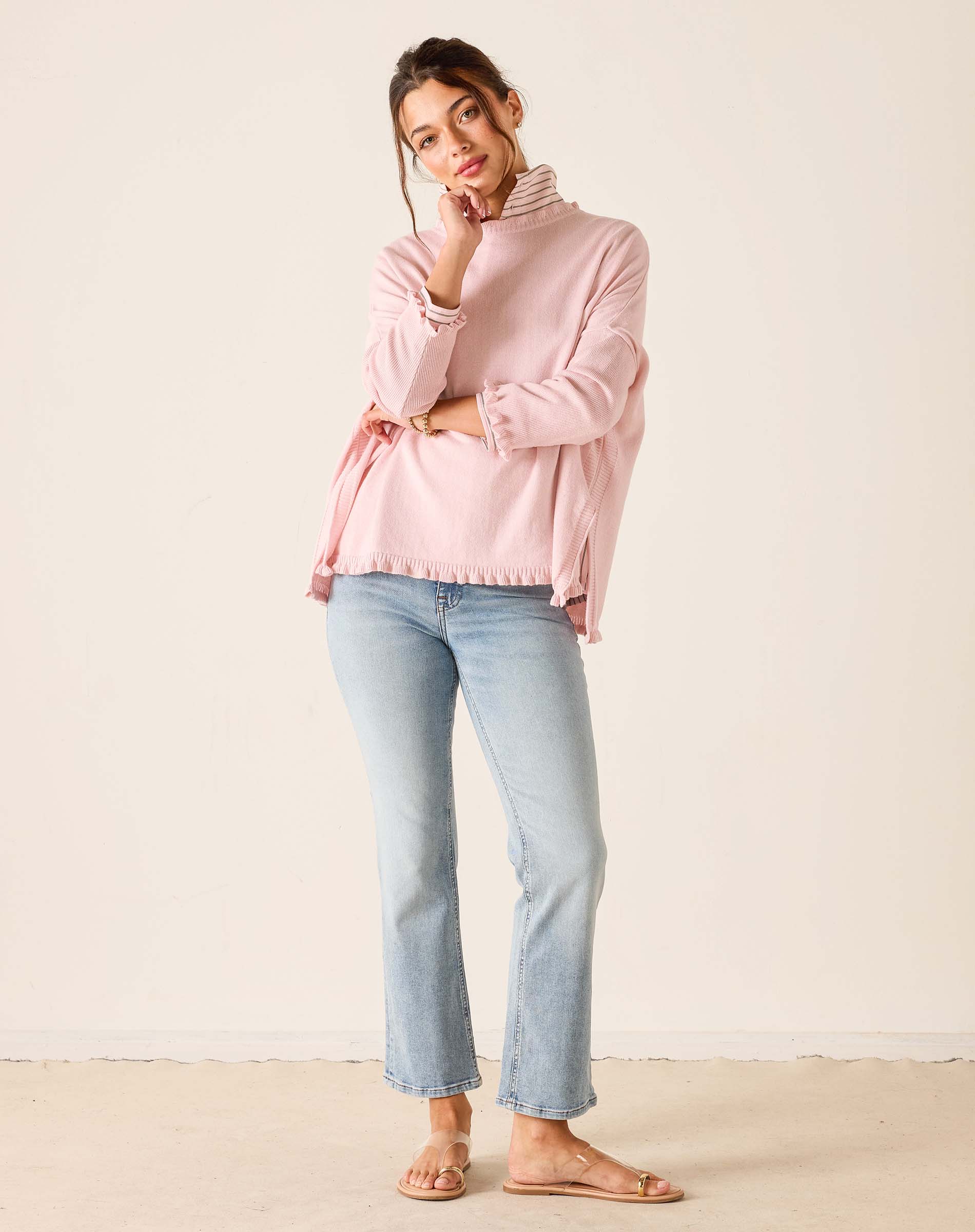 Woman wearing a pink sweater and light blue jeans against a white background