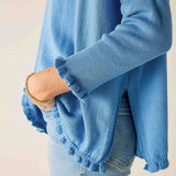 Blue sweater with ruffled hem worn by a person on a plain background