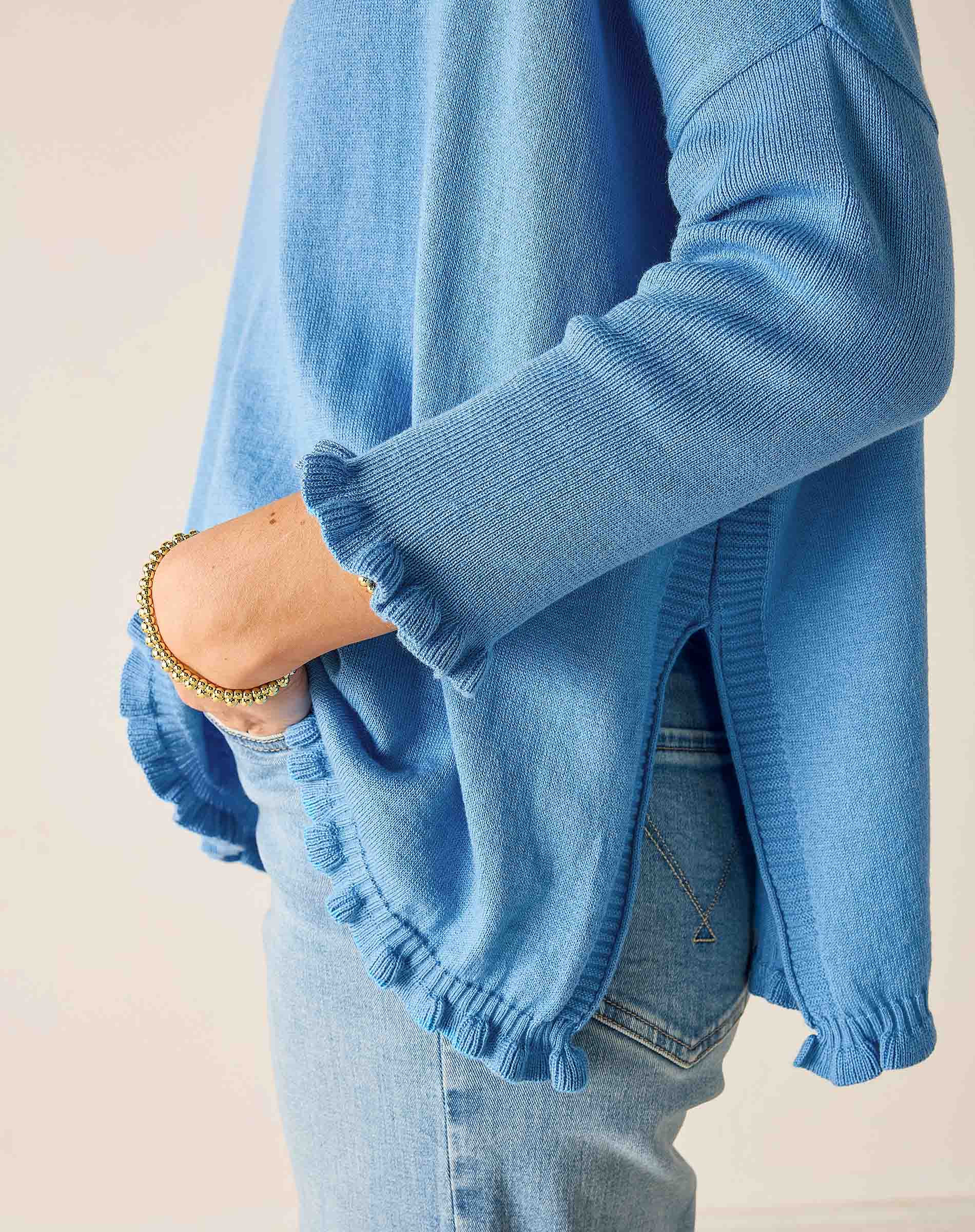 Blue sweater with ruffled hem worn by a person on a plain background