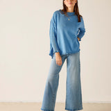 Woman wearing a blue sweater and jeans standing against a plain background