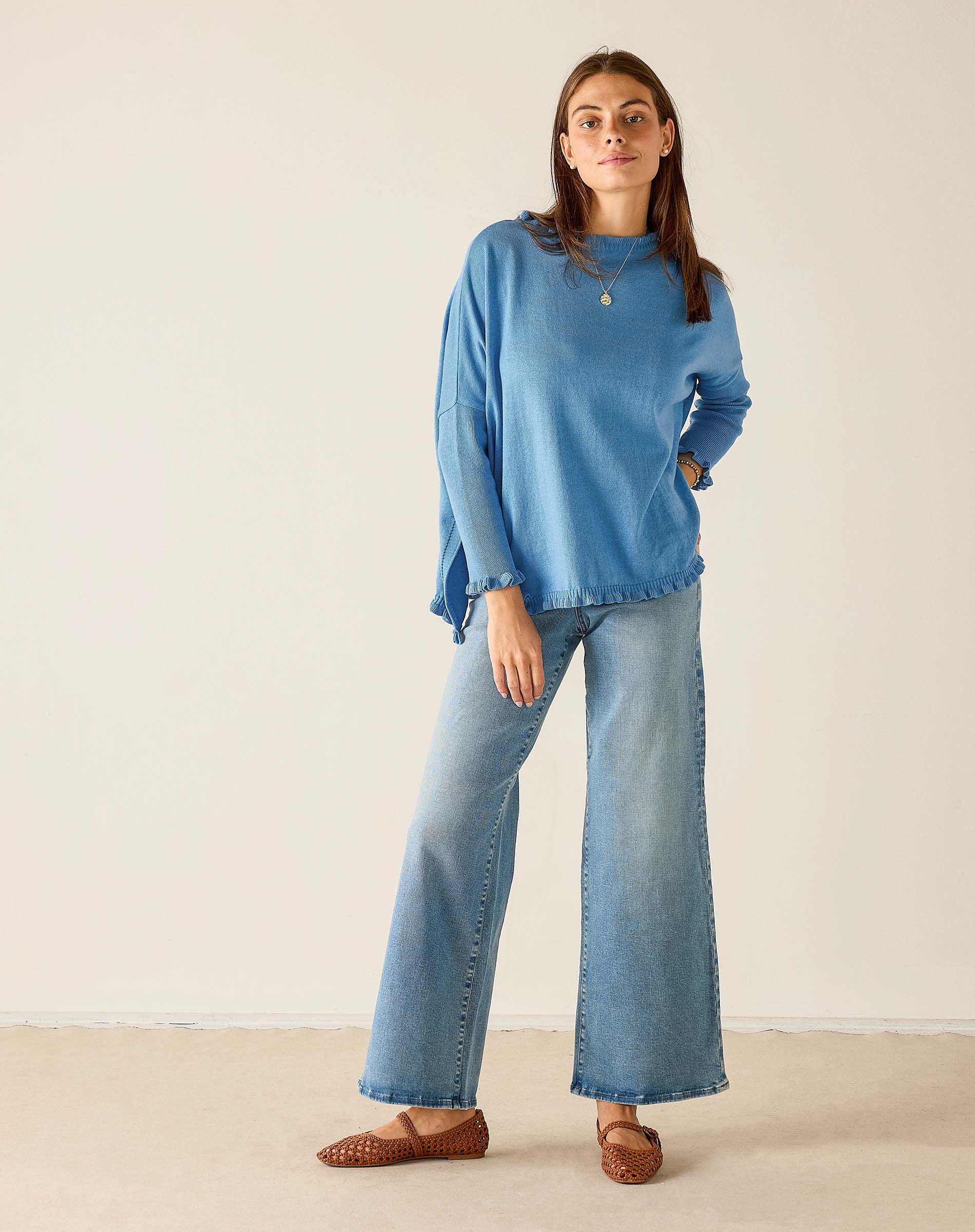 Woman wearing a blue sweater and jeans standing against a plain background