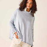 Woman wearing a light blue sweater with frayed edges on a beige background
