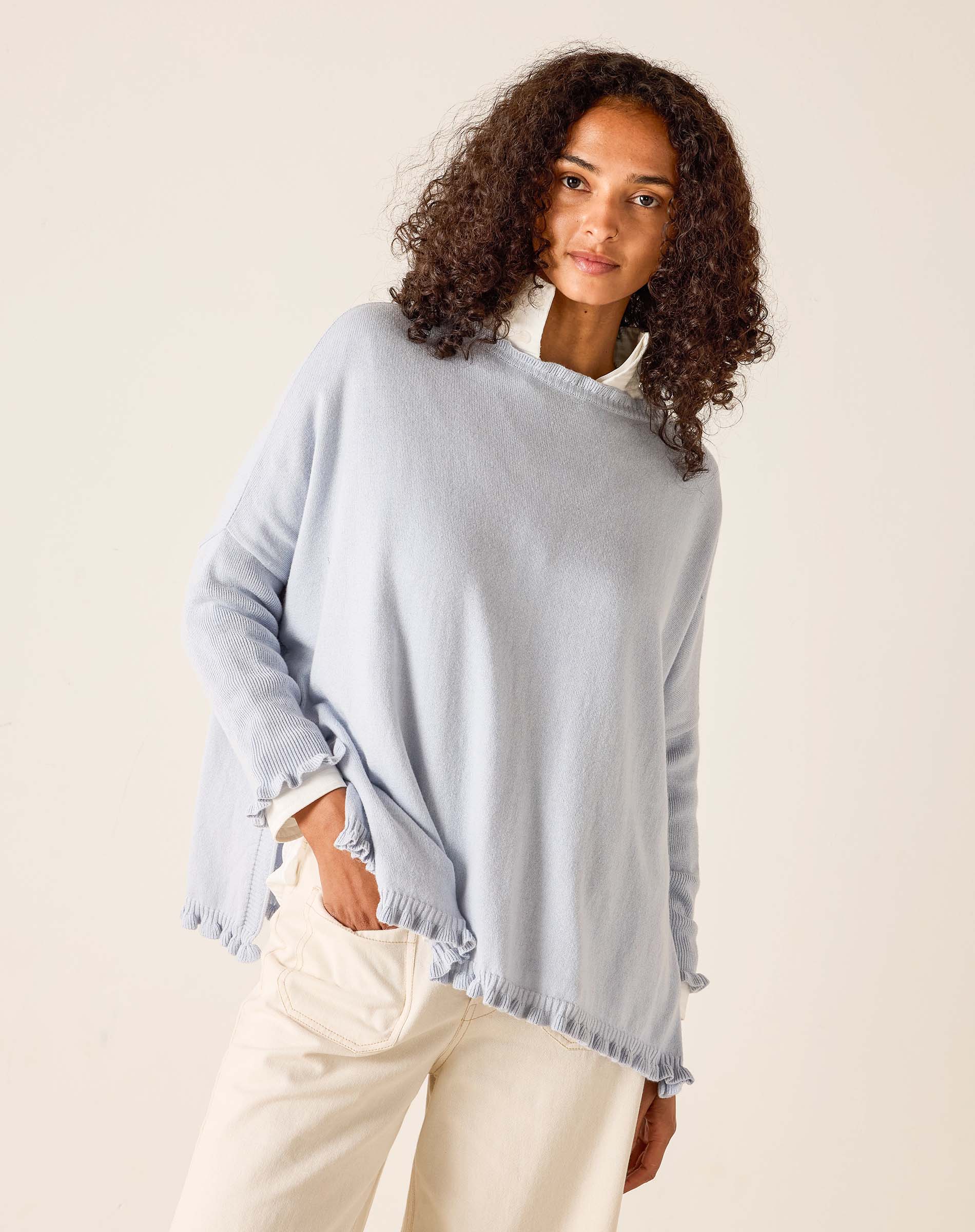 Woman wearing a light blue sweater with frayed edges on a beige background