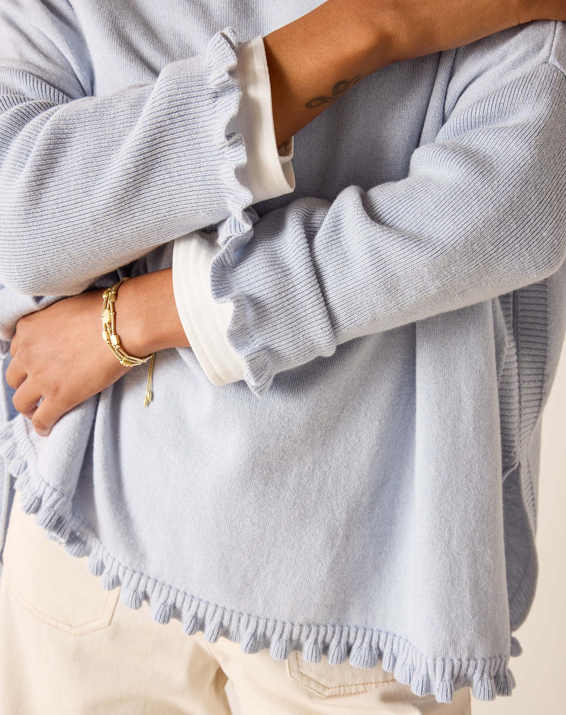 Person wearing a light gray sweater with ruffled cuffs and hem, holding a phone.