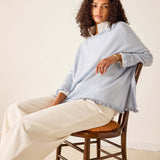 Woman sitting on a chair wearing a light blue shawl over a white outfit.