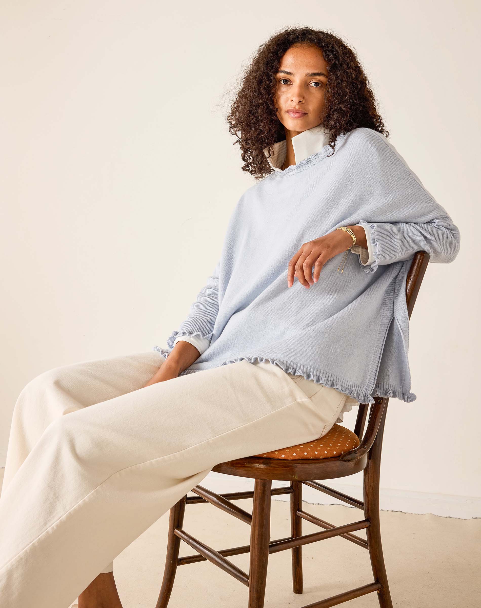 Woman sitting on a chair wearing a light blue shawl over a white outfit.