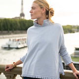 Woman wearing a light blue sweater with a blurred background of a cityscape.