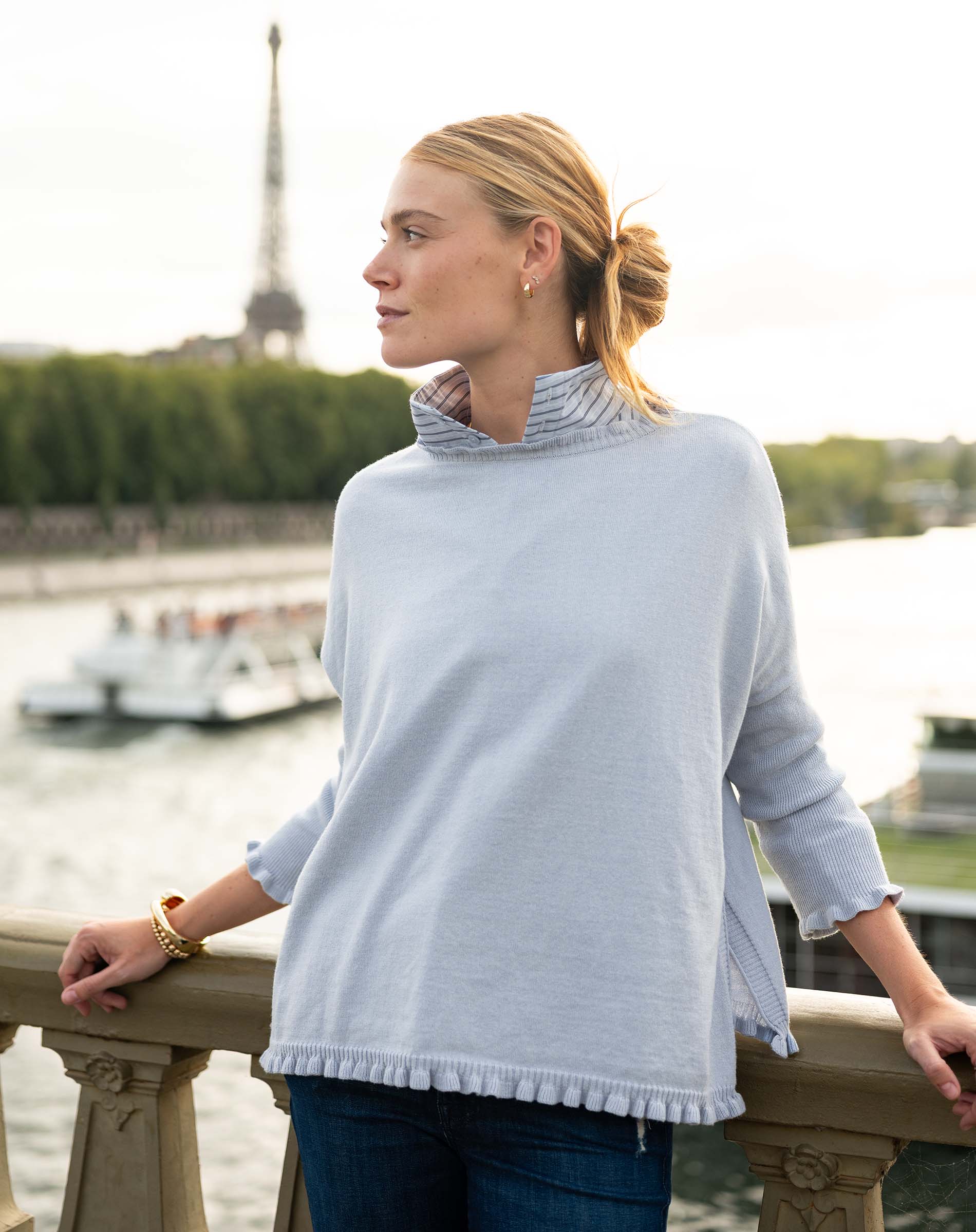 Woman wearing a light blue sweater with a blurred background of a cityscape.