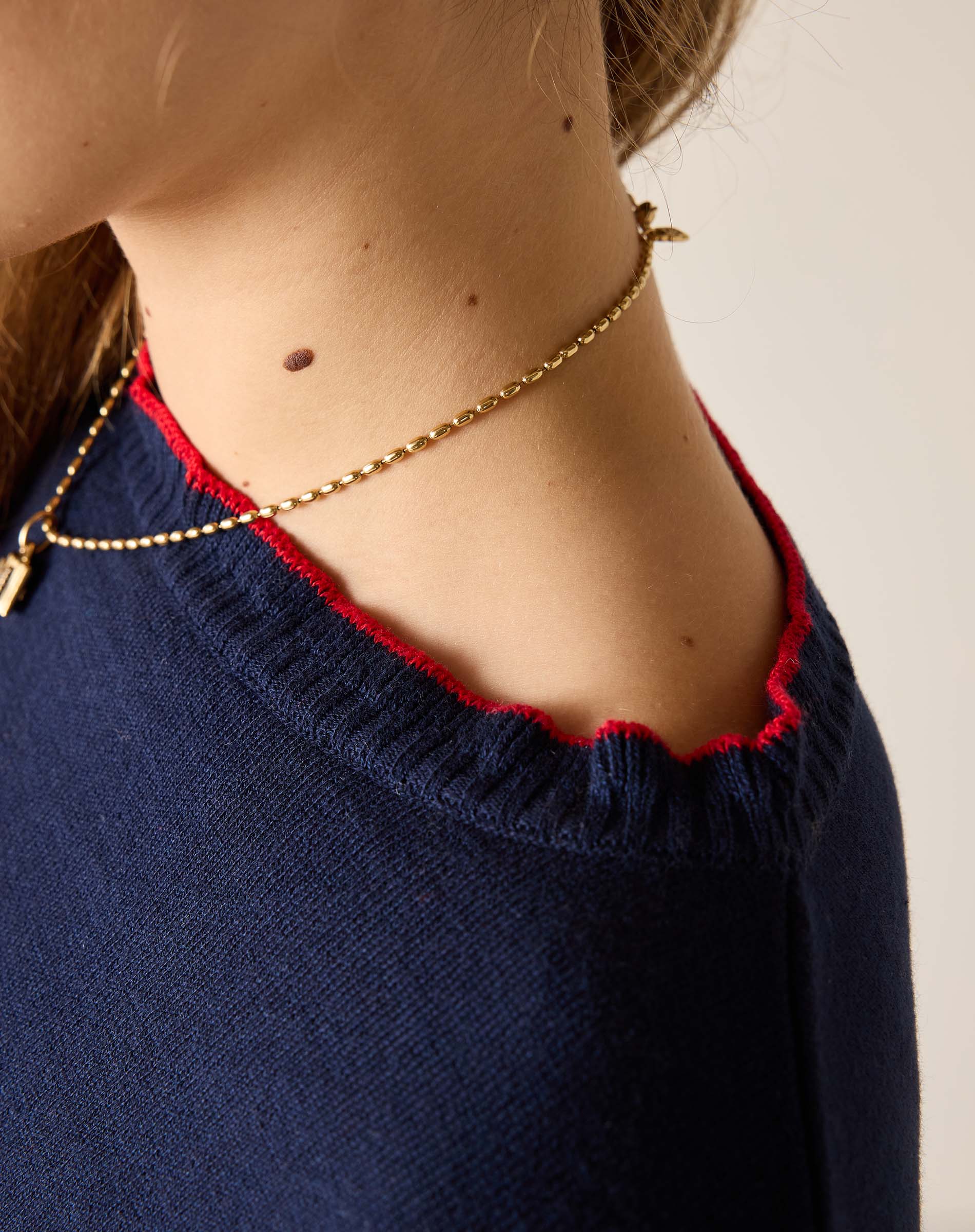 Close-up of a person wearing a gold necklace with a plain background