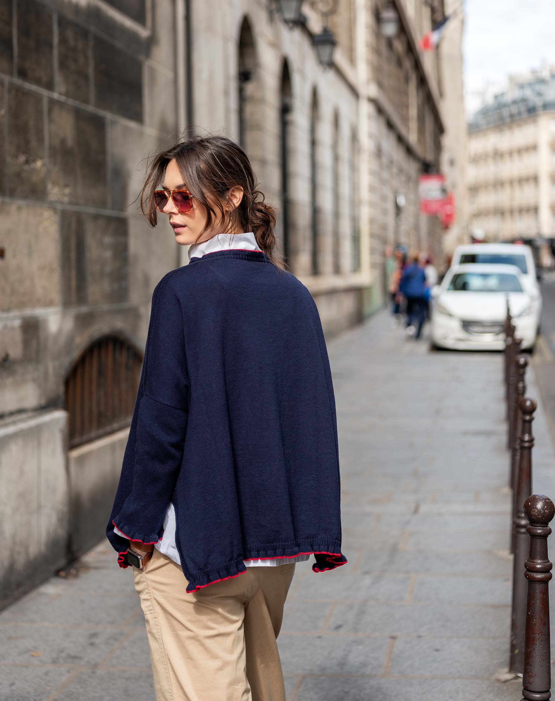 Woman walking down a city street wearing a navy blue jacket and beige pants.
