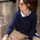 Woman wearing a navy sweater with ruffled cuffs and hem, sitting against a stone wall.