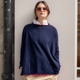 Woman wearing a navy sweater with red trim against a neutral wall.